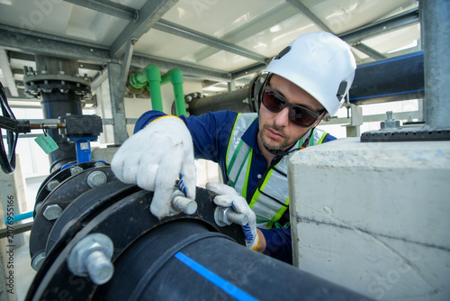 Engineer maintenance hvac cooling tower technician pipe repair wrench safety on duty adjusts bolt on industrial pipeline under hard hat and glove with care for reliable cooling water flow at plant