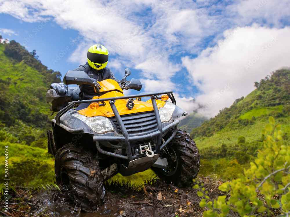 Obraz premium ATV off-road riding expedition navigates muddy mountain trail with quad bike in rugged terrain and scenic valley landscape