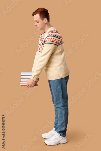 Young man holding stack of books on color background