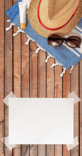 Summer Wallpaper with Straw Hat, Towel, Sunglasses, Protection Cream and White Blank Free Space Paper Sheet with Adhesive Tape on Wood Planks Surface. File with Clipping Path.