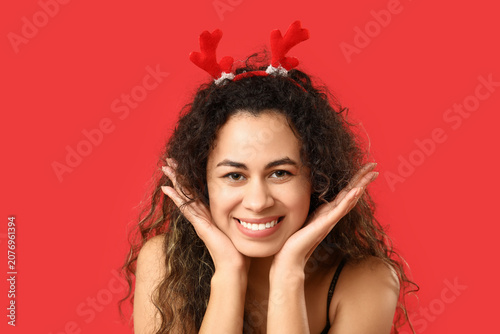 Photography Young African-American woman with Christmas reindeer antlers headband on red bac