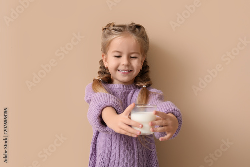 Cute little girl with glass of tasty milk on beige background