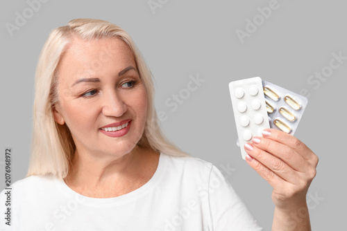Beautiful mature woman with pills and glass of water on grey background