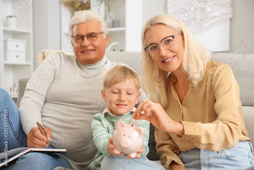 Obraz na płótnie Little boy with his grandparents putting coin in piggy bank at home