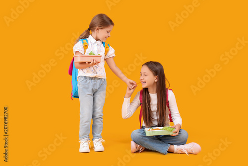 Happy girls with backpacks and lunchboxes on yellow background