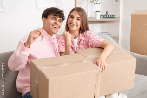 Young couple with keys and moving boxes in their new flat