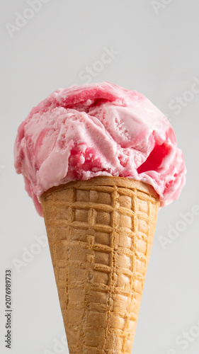 Close-up of strawberry syrup pouring over scoop of pink ice cream on a waffle cone delicious dessert texture isolated on light background.