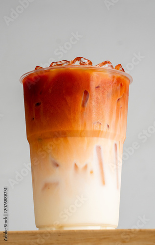 Close-up of dark red syrup or tea being poured into plastic cup filled with milk and ice creating a swirling layer effect isolated on light neutral background.