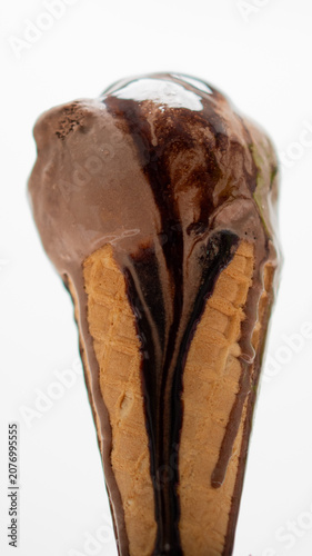 Close-up delicious chocolate ice cream cone topped with rich chocolate syrup melting down the waffle cone isolated on white background.