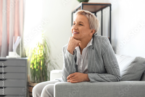 Happy mature businesswoman sitting on sofa in office