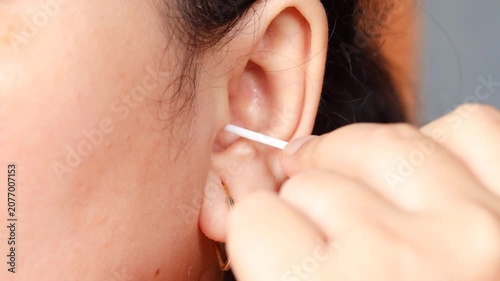 Close up of a young Asian woman cleaning her ear with a cotton swab for personal healthcare and ear disease prevention.