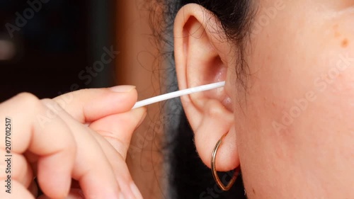 Close up of a young Asian woman cleaning her ear with a cotton swab for personal healthcare and ear disease prevention.