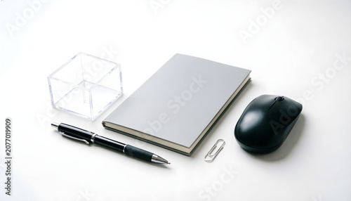 Minimalist office desk workspace with notebook, computer mouse, pen, paper clip, and transparent organizer on white background