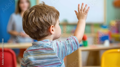 Little boy raising his hand to answer in a classroom