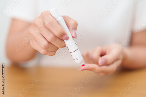 Photos Hand using lancet pen on finger with Blood drop glucose testing or Diabetes checking by digital blood glucose meter