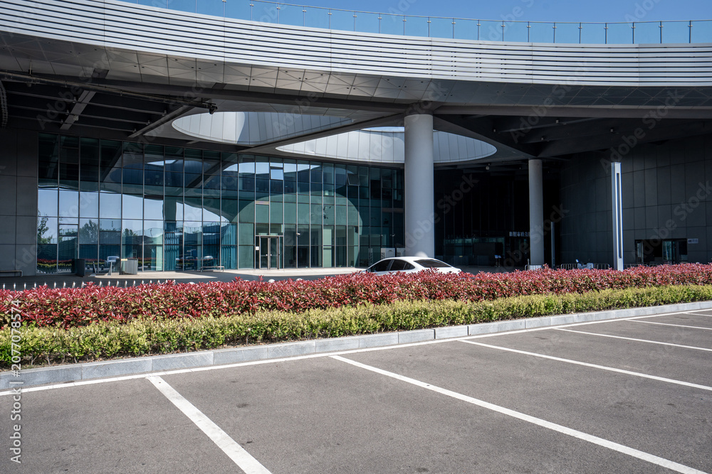 Obraz premium Modern building entrance with glass curtain wall and empty parking lot under clear sky