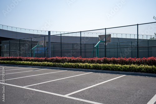 Tableau sur toile Empty outdoor basketball court adjacent to paved parking lot with green shrubs a