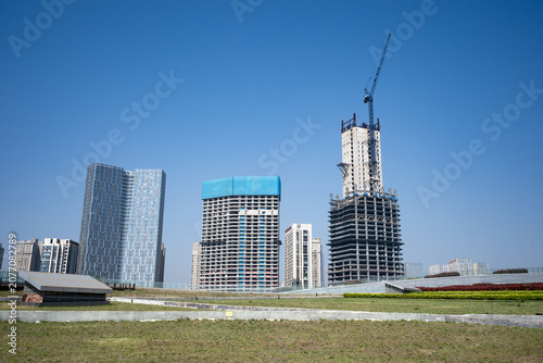 Modern high-rise buildings under construction in a new urban district with cranes against clear blue sky