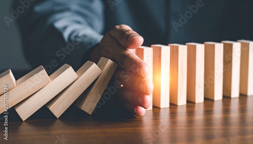 Hand stopping falling wooden domino blocks, symbolizing risk management, crisis prevention, business continuity, resilience, and strategic decision making.