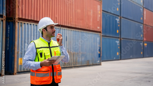 Port worker using a radio transceiver to control a crane loading container boxes onto a cargo ship, representing sea transportation and logistics business concepts