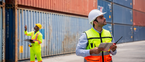 Fotografía Port worker using a radio transceiver to control a crane loading container boxes