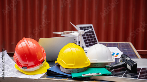 Bright yellow safety hard hat placed on dark soil with a blurred industrial background of container stacks, cranes, and heavy equipment at a shipping port