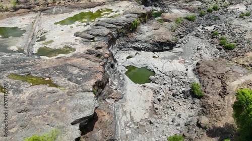 High-resolution aerial drone photograph of a rocky riverbed featuring natural rock formations, shallow green water pools, and a dry seasonal waterfall.