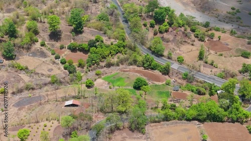 A high-resolution aerial drone photograph of a winding mountain road featuring multiple hairpin bends through a dry deciduous forest