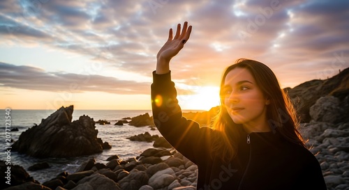 Young woman waving hello at sunset on rocky beach