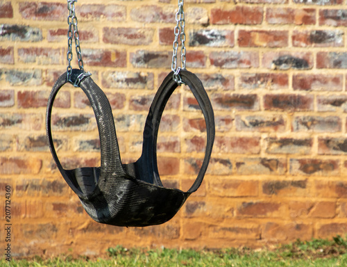 An empty child's swing made from an old car tyre hangs unused in an empty playground