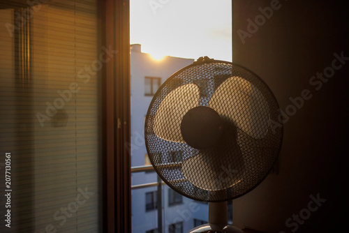 Obraz na plátně An electric fan standing inside a room at sunrise on a hot summer morning, circulating cool air to improve ventilation during an extreme heatwave