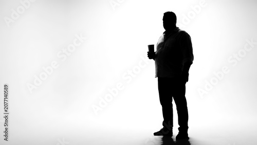 Silhouette of man standing and holding cup against bright white high-key background with large copy space, minimalist studio portrait for design and editorial use