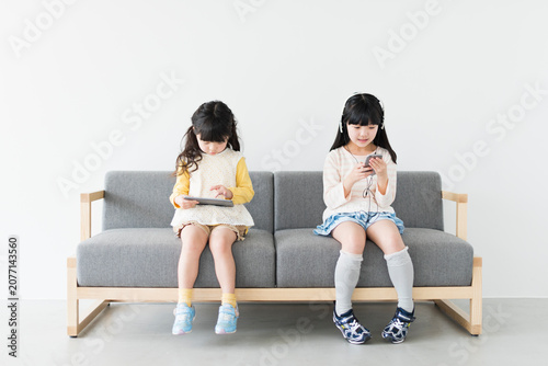 ソファでタブレットとスマートフォンを使う姉妹