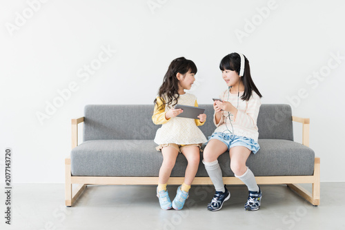 ソファでタブレットとスマートフォンを使う姉妹