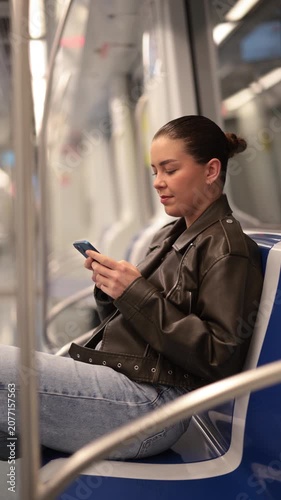  Young woman sitting with mobile phone riding in subway car