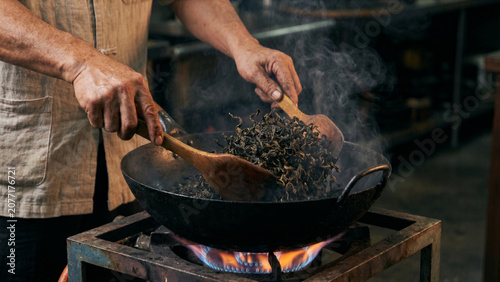 Close up of Taiwanese tea master hand firing oolong tea leaves in heated iron wok smoke photo