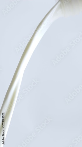 4K Close-up of fresh white milk or cream pouring smoothly from bottle mouth against on white background.