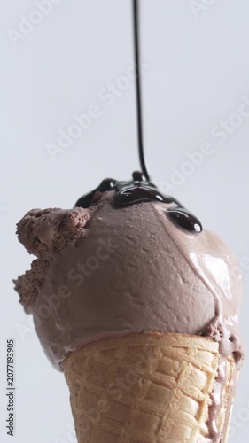 4K Close-up delicious chocolate ice cream cone topped with rich chocolate syrup melting down the waffle cone isolated on white background.
