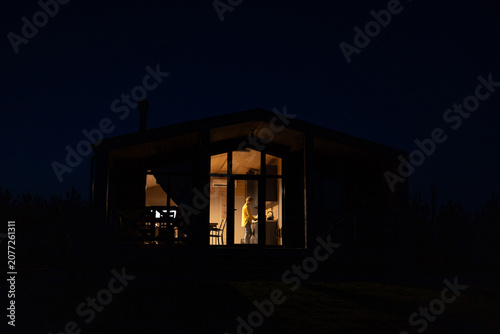 Foto A solitary woman stands inside a brightly lit cabin at night, preparing food in