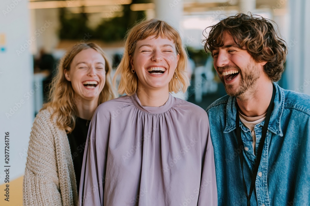 Naklejka premium Three diverse office colleagues laughing during a candid conversation in a modern workspace for corporate culture and workplace wellness content
