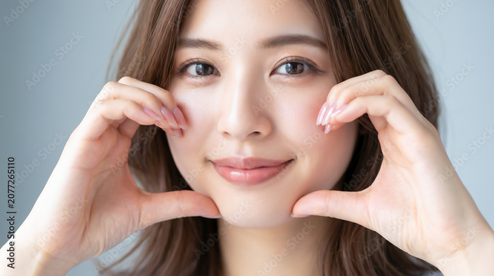 Fototapeta premium ほっぺハートを作って笑顔を見せる若い女性
