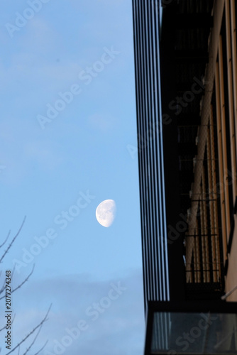 Foto Low angle vertical shot of a gibbous moon in a pale blue daylight sky next to a modern building facade with vertical lines