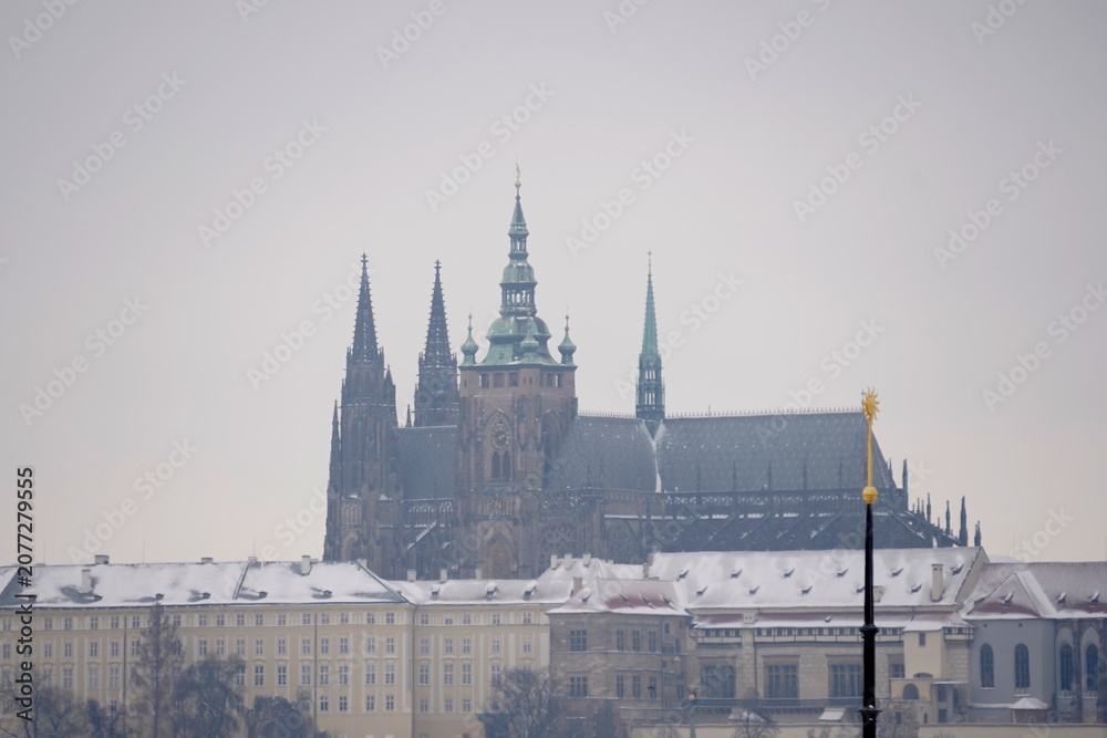 Obraz premium Magnificent historical castle complex featuring majestic gothic cathedral towers rises above snow covered palace buildings under a pale overcast winter sky, capturing a cold seasonal scene.