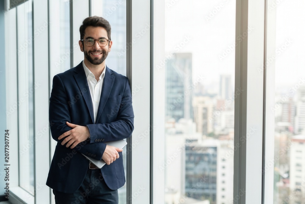 Fototapeta premium Businessman holding a tablet and smiling, standing by a corporate office window