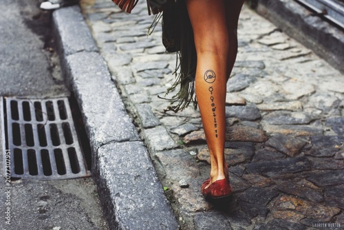 Obraz na płótnie Woman walking on cobblestone street with tattoos and red shoes