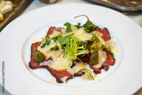 Carpaccio with parmesan, arugula, and capers on a white plate