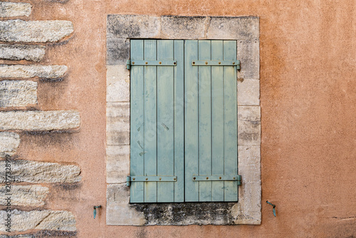 Turquoise wooden shutter on a weathered peach plaster wall in France
