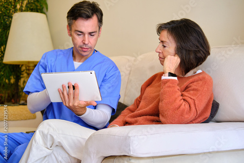 Fotografie Caregiver man consulting senior woman using digital tablet at home