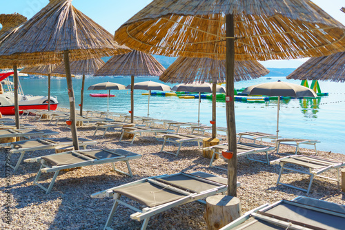 Fotografía Traditional straw parasols and empty sun loungers on the pebble beach overlookin