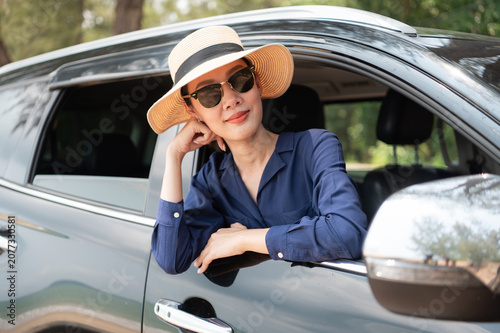 A joyful traveler is feeling the coastal breeze as she drives her SUV. Dressed in a chic sun hat and sunglasses and the calm ocean backdrop completing this perfect getaway
